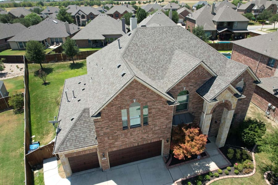 Completed architectural shingle roof on a two-storey Texas brick home, aerial view